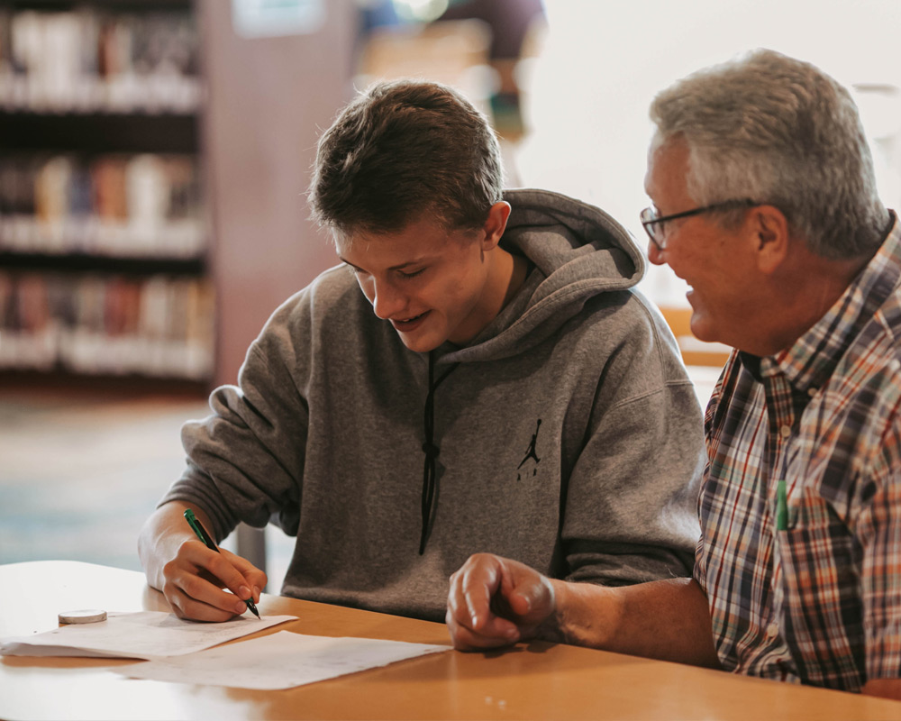 High school male doing math homework with math teacher in media center