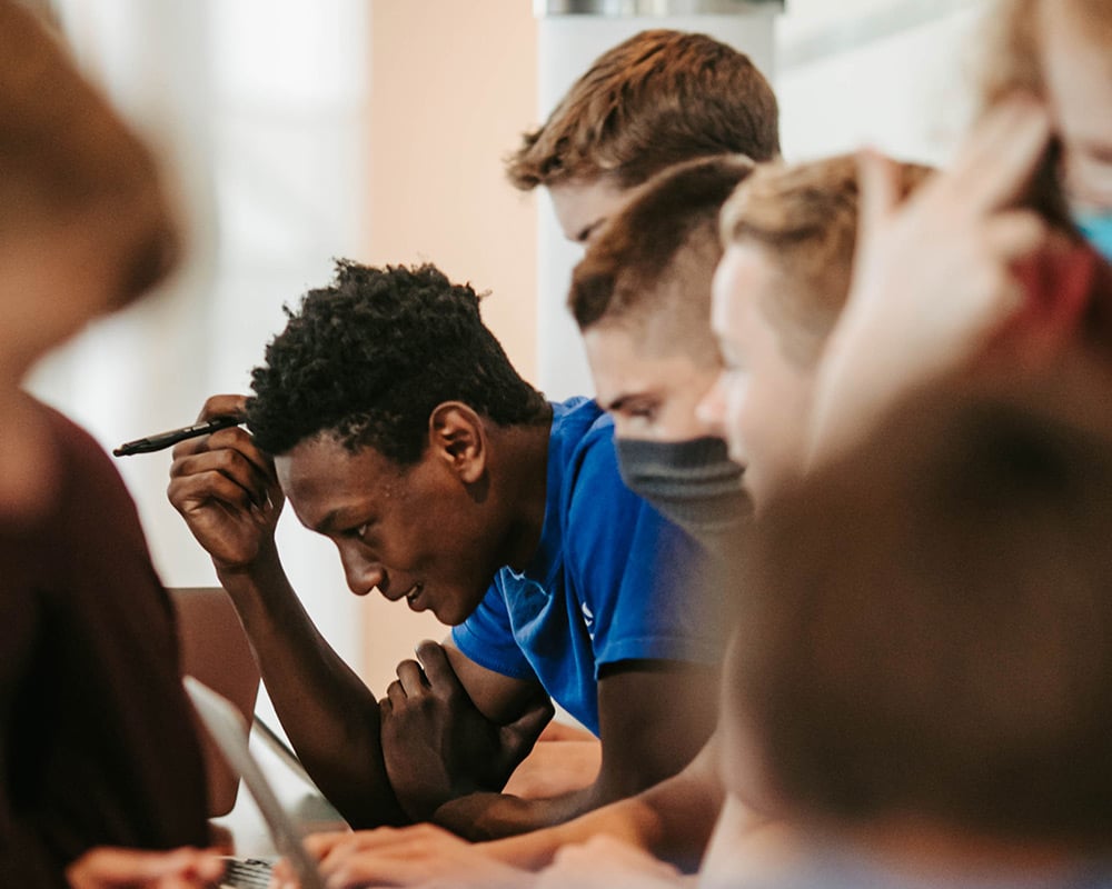 Boy with pen leaning forward in row of high school boys studying together