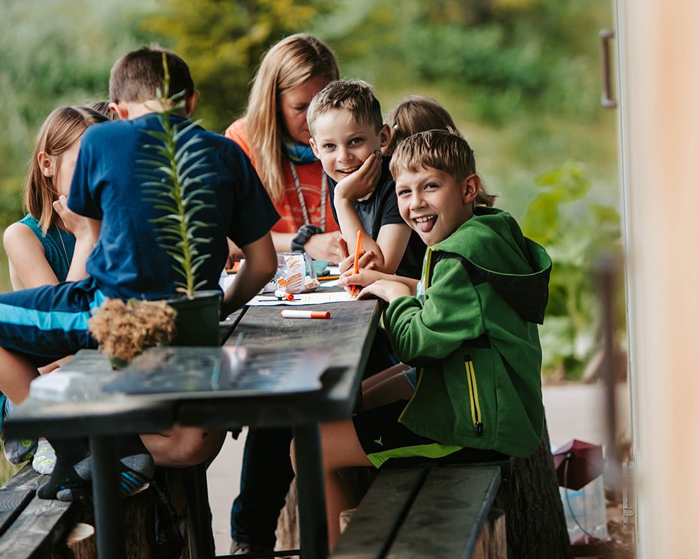 Forest School kids studying at table outside, smiling at camera