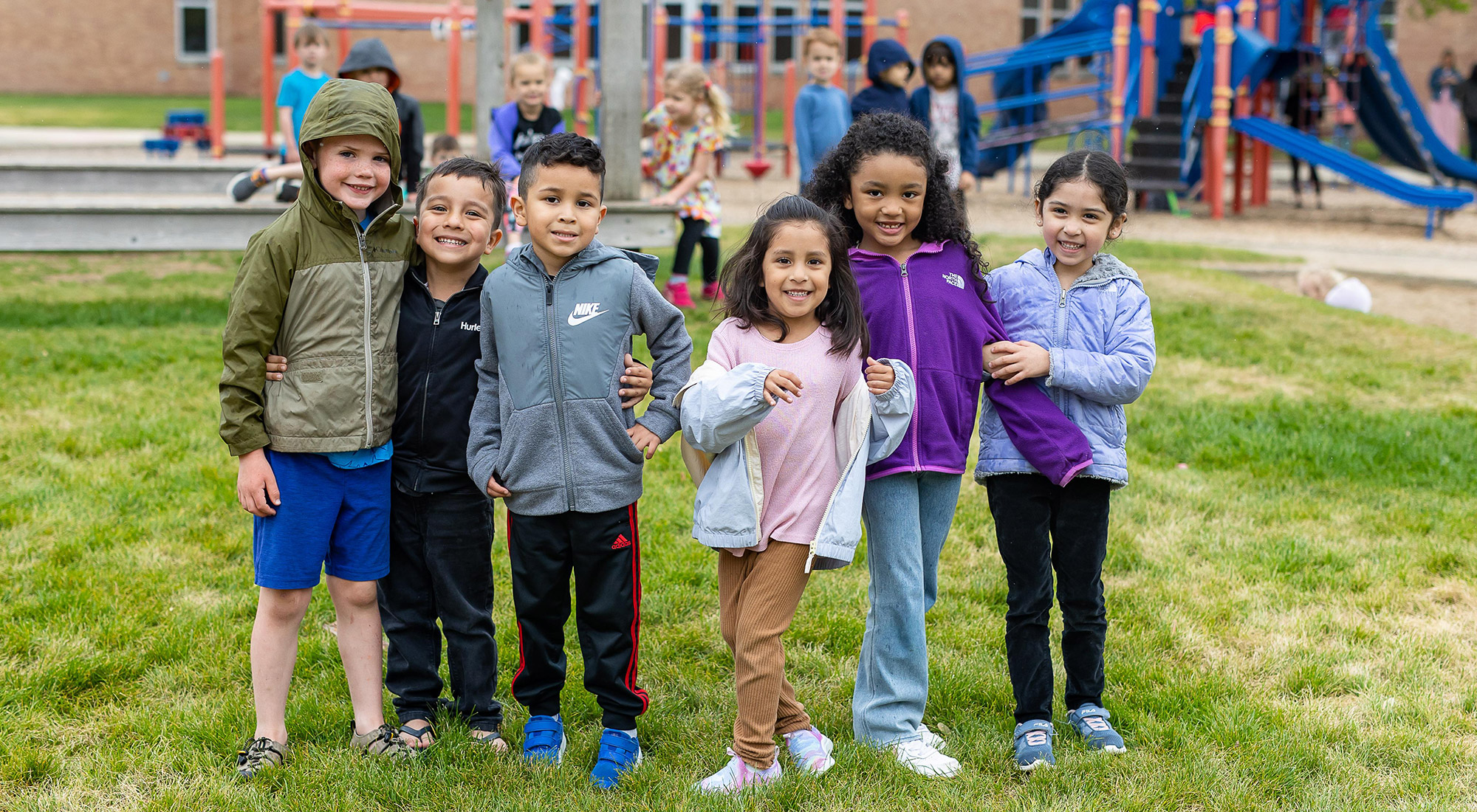 6 elementary students standing together on the Rose Park playground, all looking at the camera and smiling