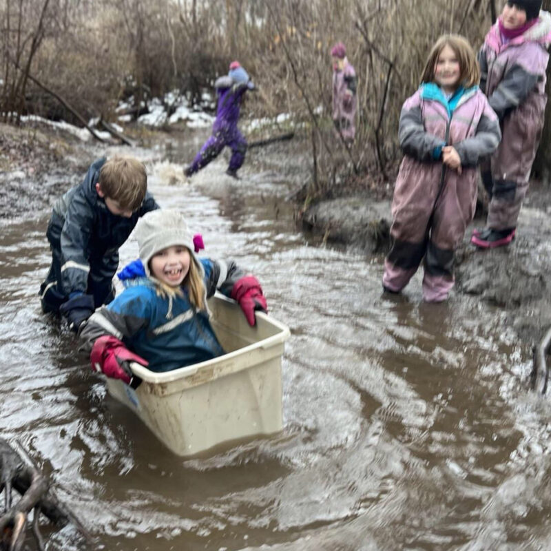 Forest School girl sitting in Rubbermaid tub being pushed down a small river