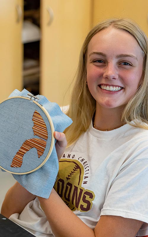High school art student smiling and holding up embroidery art in a hoop