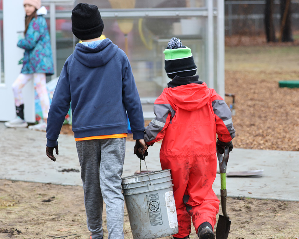 Two boys carrying a bucket, helping each other outside Rose Park Ranch