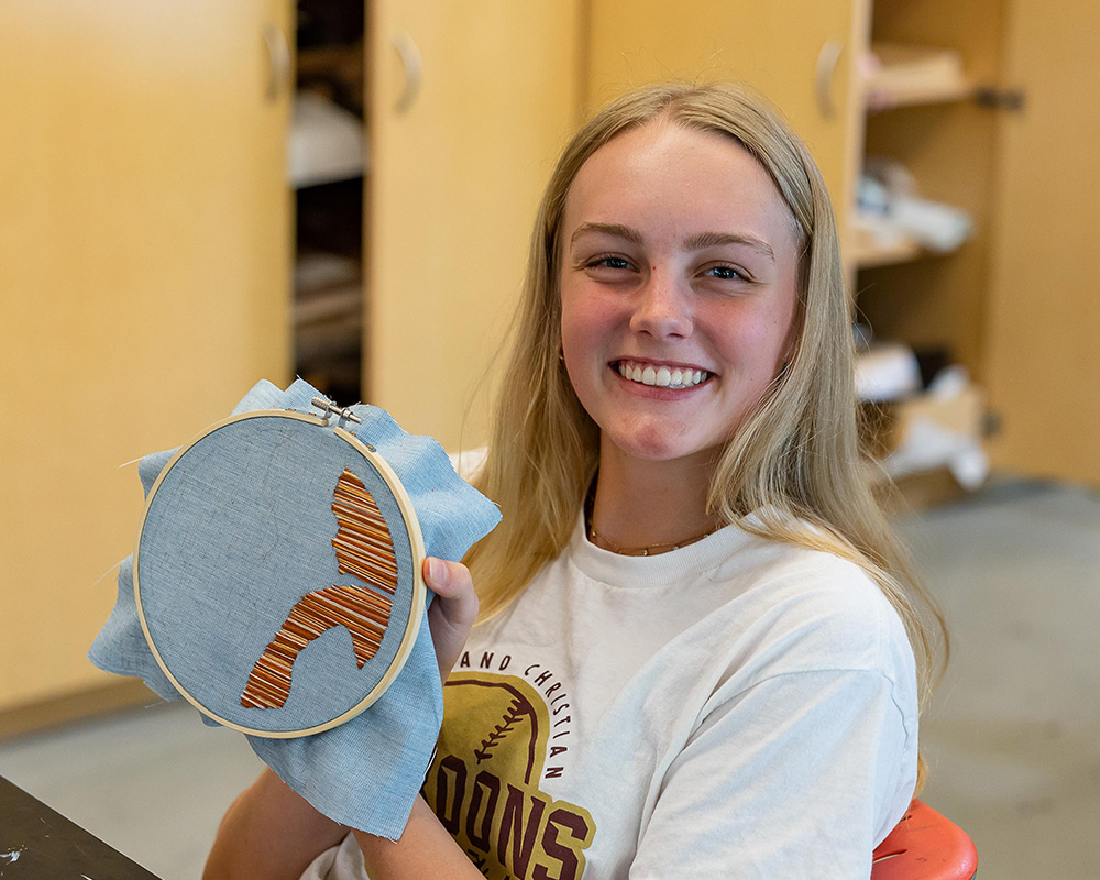 HS female art student holding her textile art up and smiling at the camera