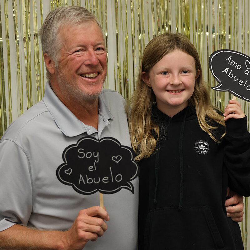 Grandpa and grandaughter holding abuelo signs and smiling at the camera