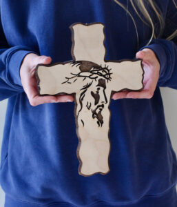Hands holding a small cross with the imprint of Jesus in darker color