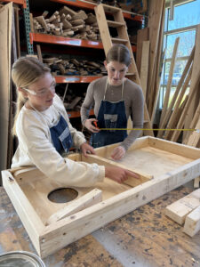 Two high school girls measuring a corn hole base from the bottom