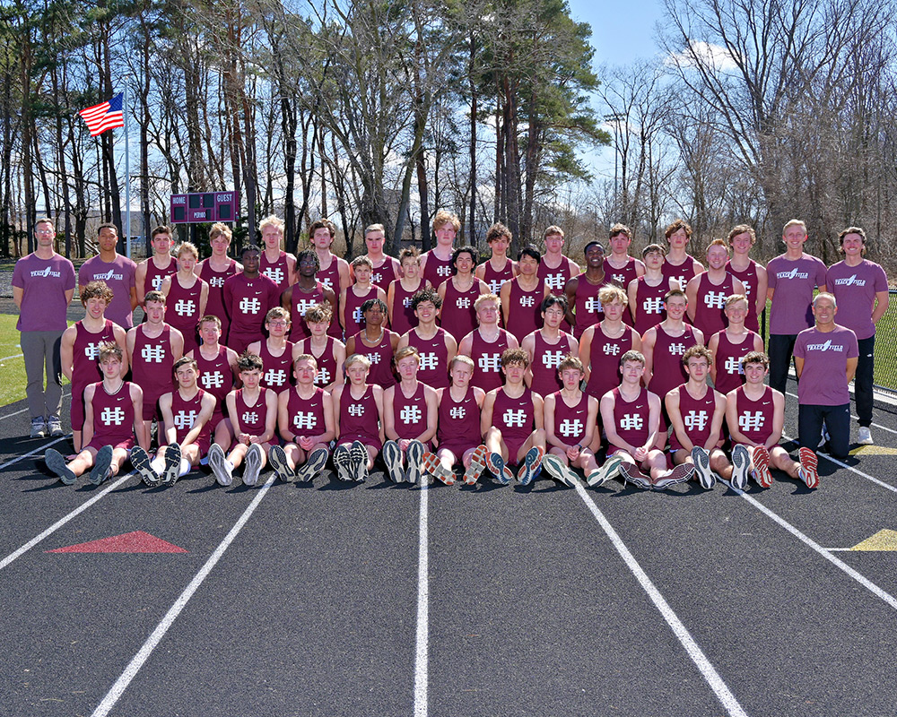 Boys track team dressed in maroon singlets and shorts posing outside on the track for the camera