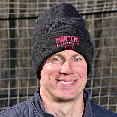Girls JV soccer coach standing in front of the soccer goal and smiling at the camera