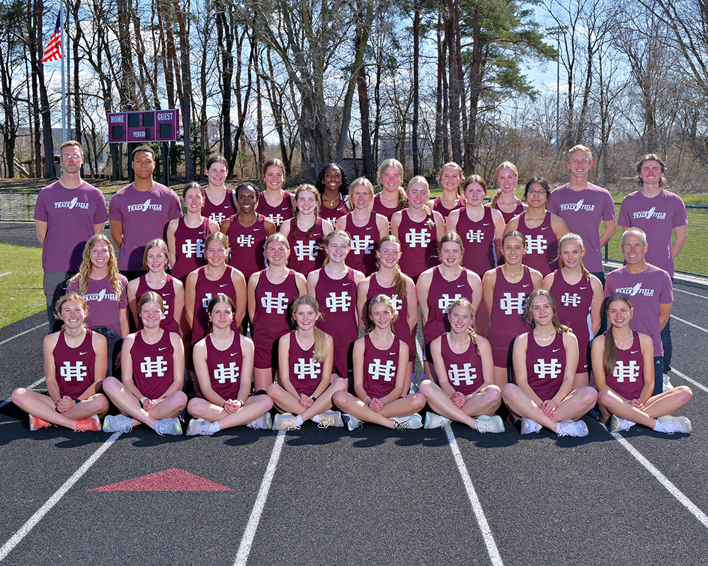 Girls track team wearing maroon tops and shorts uniforms posing outside on the track for the camera