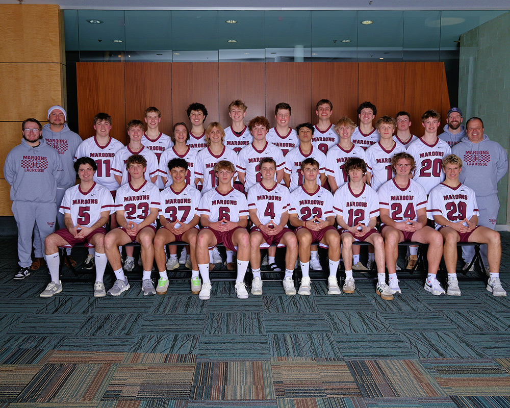 Varsity boys lacrosse team lined up and smiling at the camera.