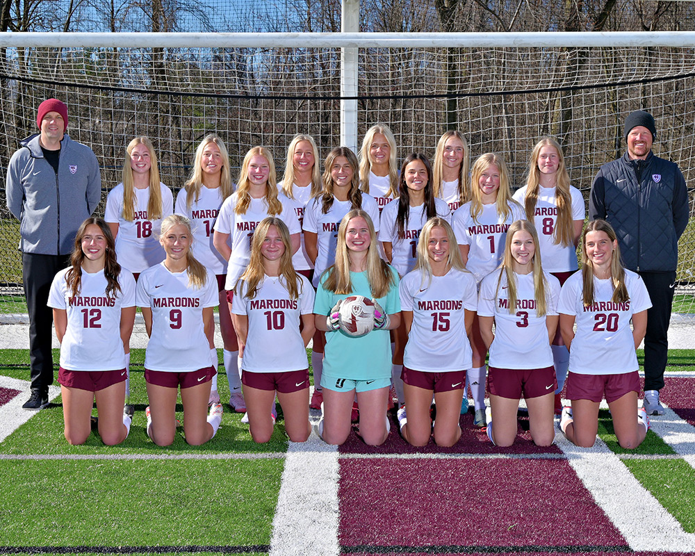 Girls varsity soccer team standing in front of a soccer goal and smiling at the camera