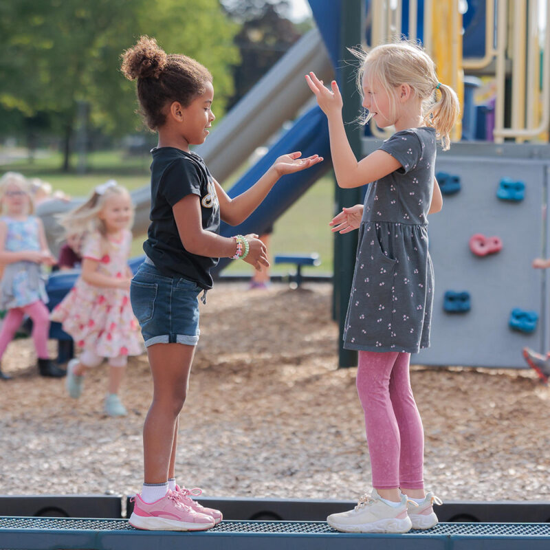 Two elementary girls playing clapping games on the playground.