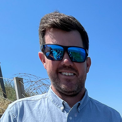 Joe Baillargeon smiling with sunglasses on outside under a blue sky.