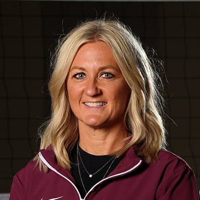 Coach Leeuw smiling at the camera in front of a volleyball net.