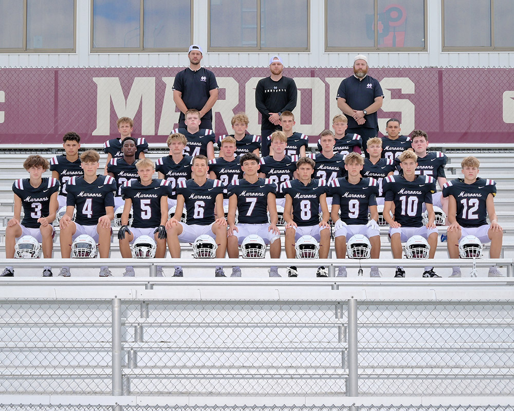 JV football team looking at the camera, seated on the bleachers in their uniforms.