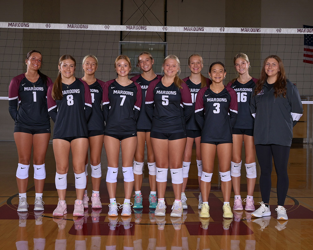 JV girls volleyball team smiling at the camera, wearing black uniforms.