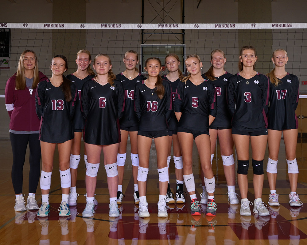 Freshmen girls volleyball team smiling at the camera, wearing black uniforms.