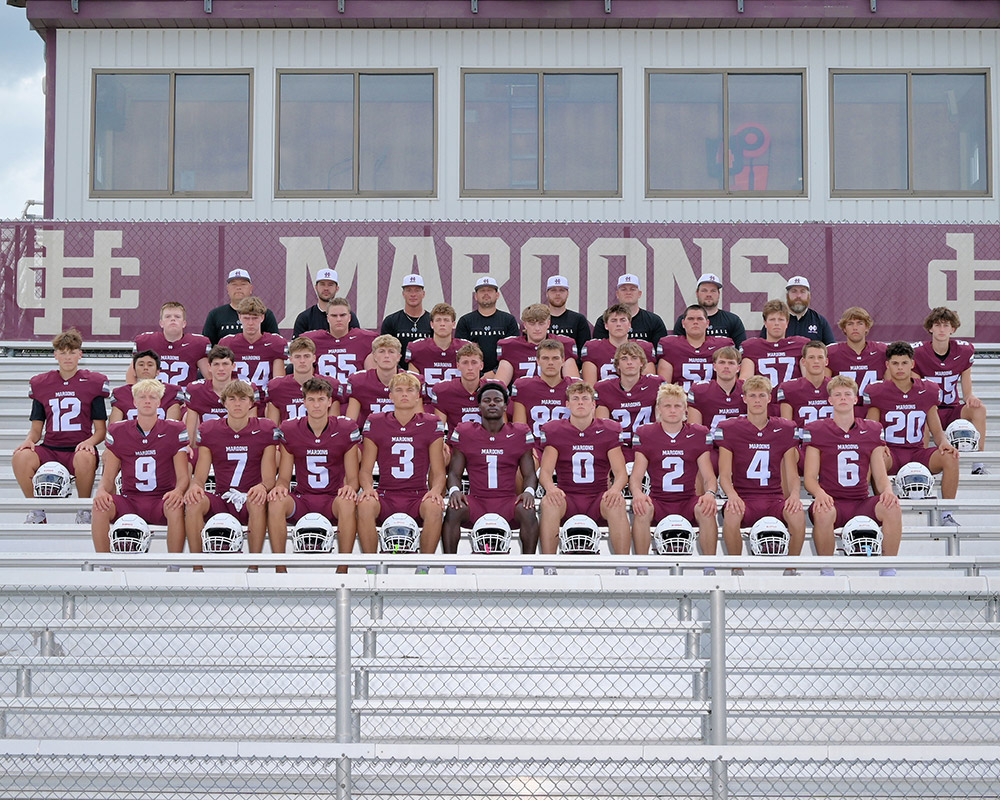 Varsity football team staring at the camera, seated in uniform on the bleachers