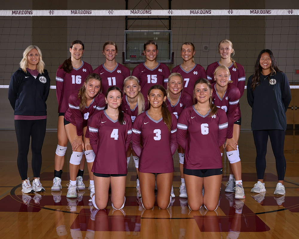 Girls varsity volleyball team smiling at the camera, wearing maroon jerseys.