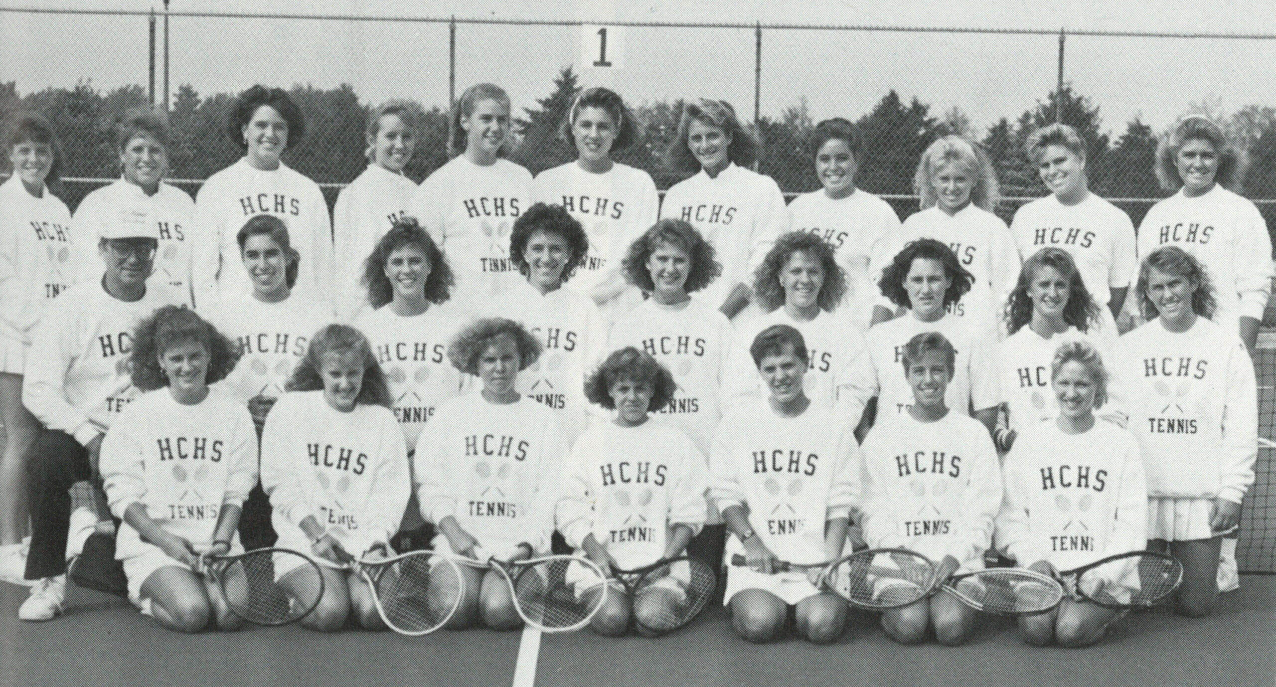 Black and white yearbook tennis team photo, with three rows of female tennis players in white HCHS sweatshirts.