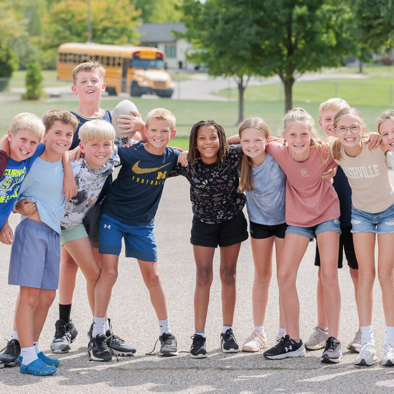 Pine Ridge students standing together and smiling at the camera, dressed in shorts on the playground