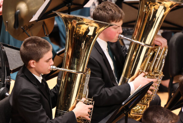 Two tuba players playing, dressed in black suits for the concert