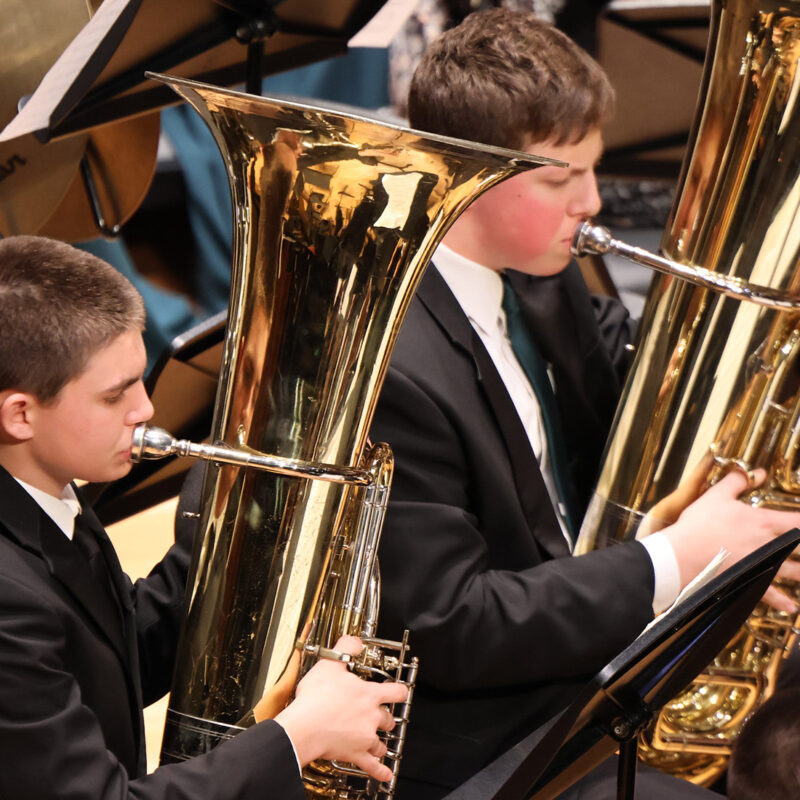 Two tuba players playing, dressed in black suits for the concert