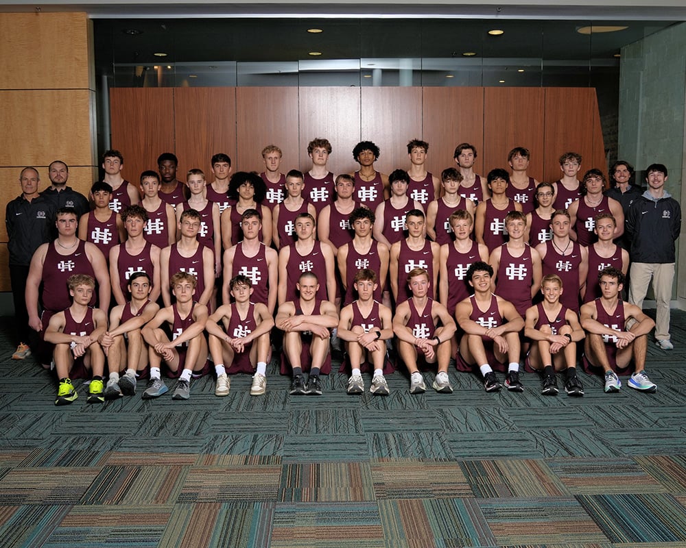 Boys track team dressed in maroon singlets and shorts posing inside for the camera