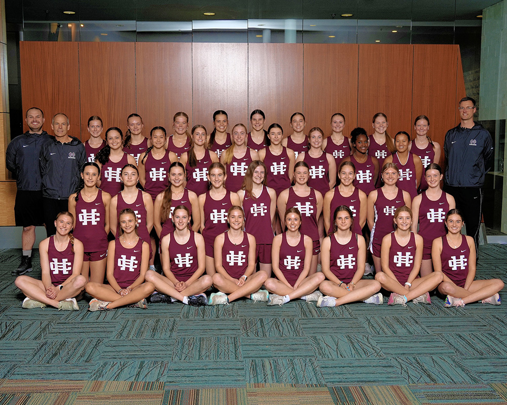 Girls track team in maroon uniforms smiling at the camera, inside