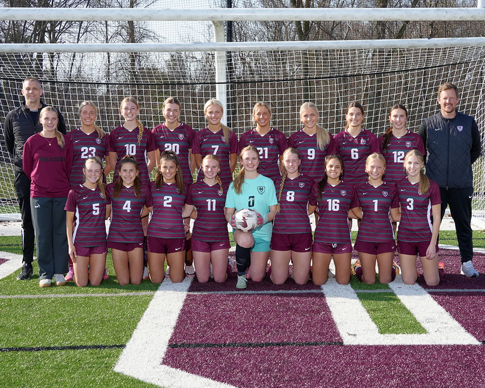Girls varsity soccer team standing in front of a soccer goal and smiling at the camera