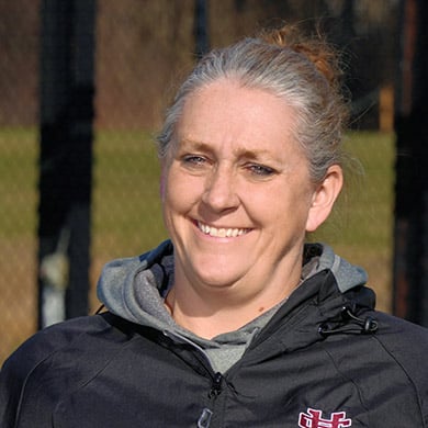 Girls varsity softball coach posing outside, smiling at the camera.