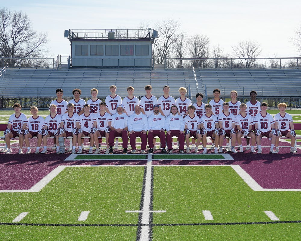 Varsity boys lacrosse team lined up and smiling at the camera.