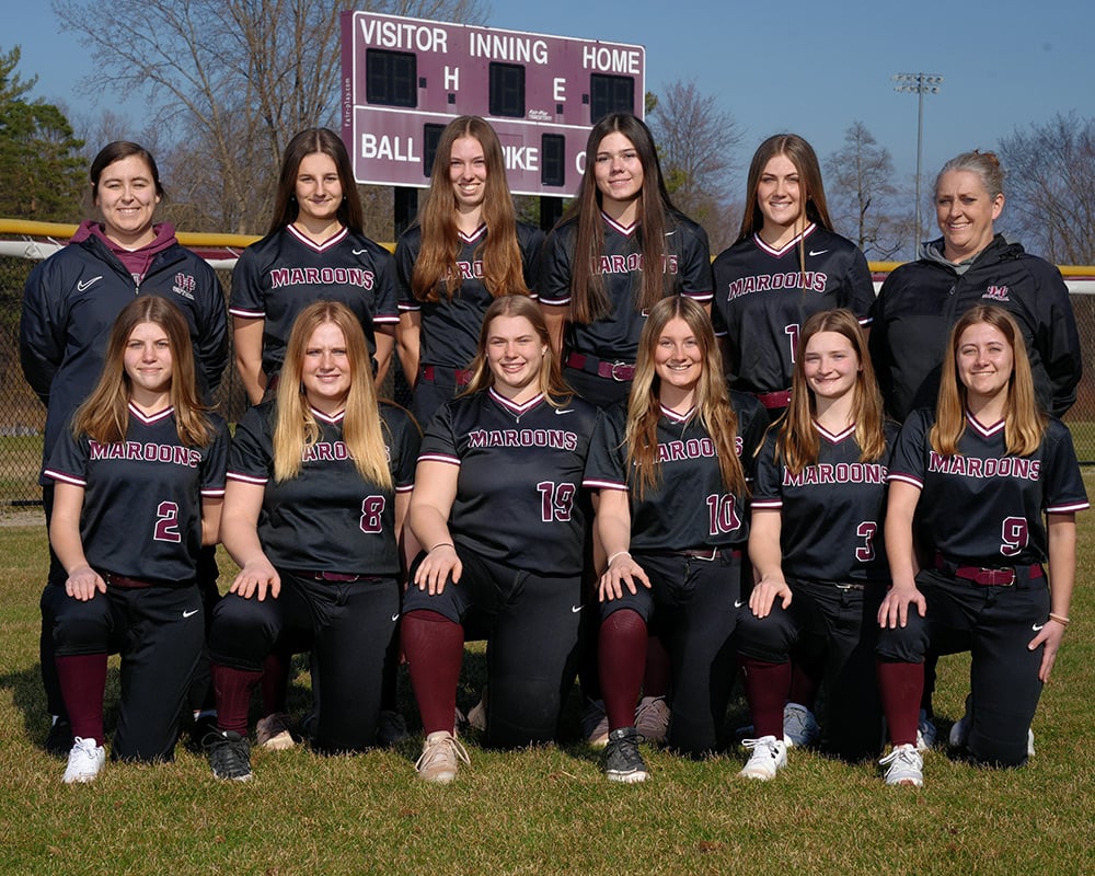 Varsity softball team in black uniforms, posing outside and smiling for the camera